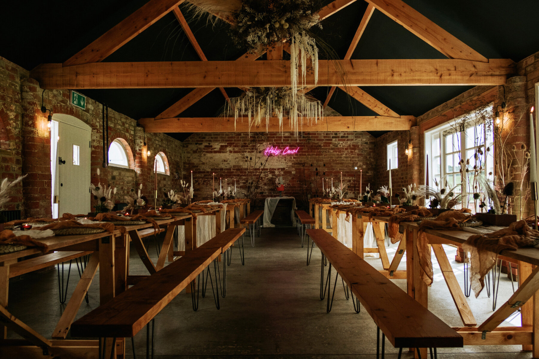 Rustic wedding venue featuring exposed brick walls, wooden beams, and long communal tables adorned with elegant floral centerpieces.