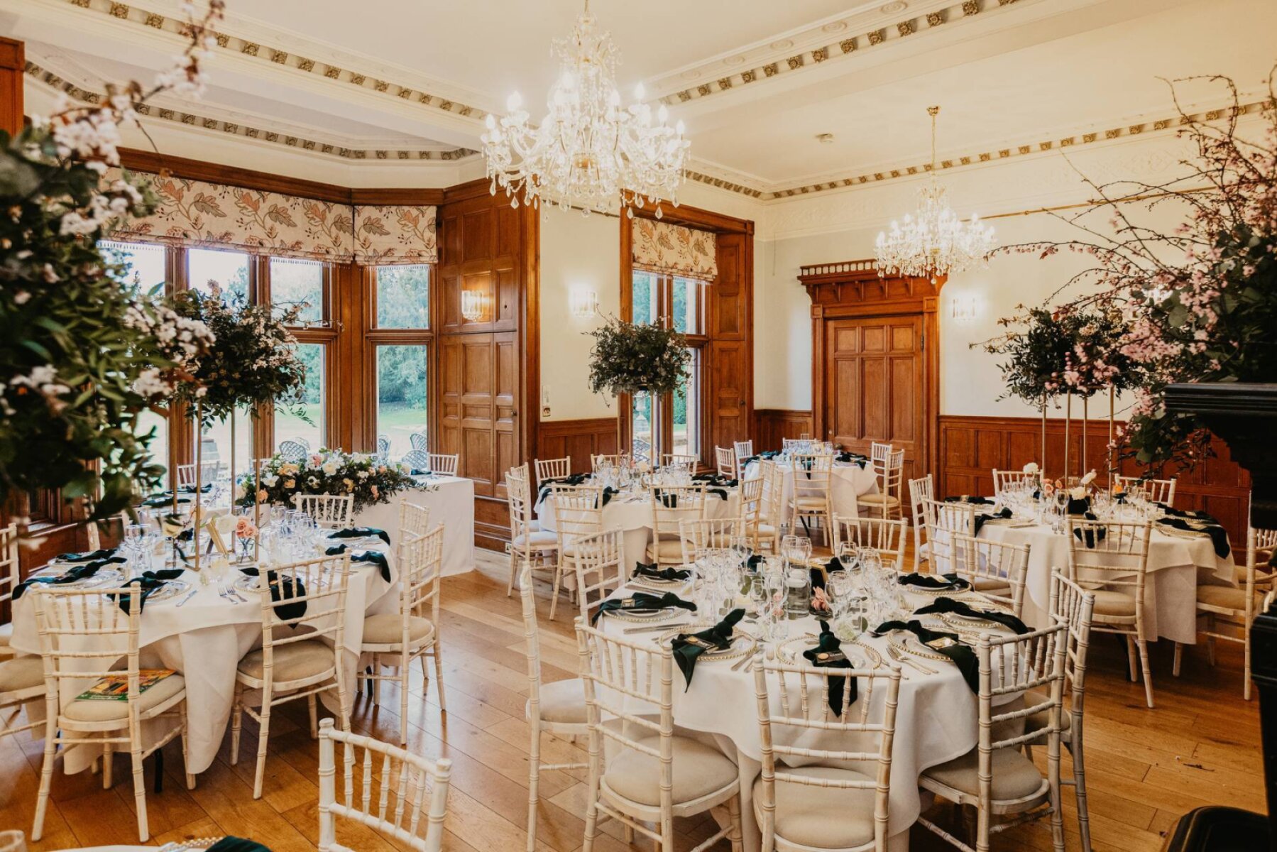 Elegant reception space featuring round tables adorned with dark green accents, surrounded by chic floral arrangements and vintage chandeliers.
