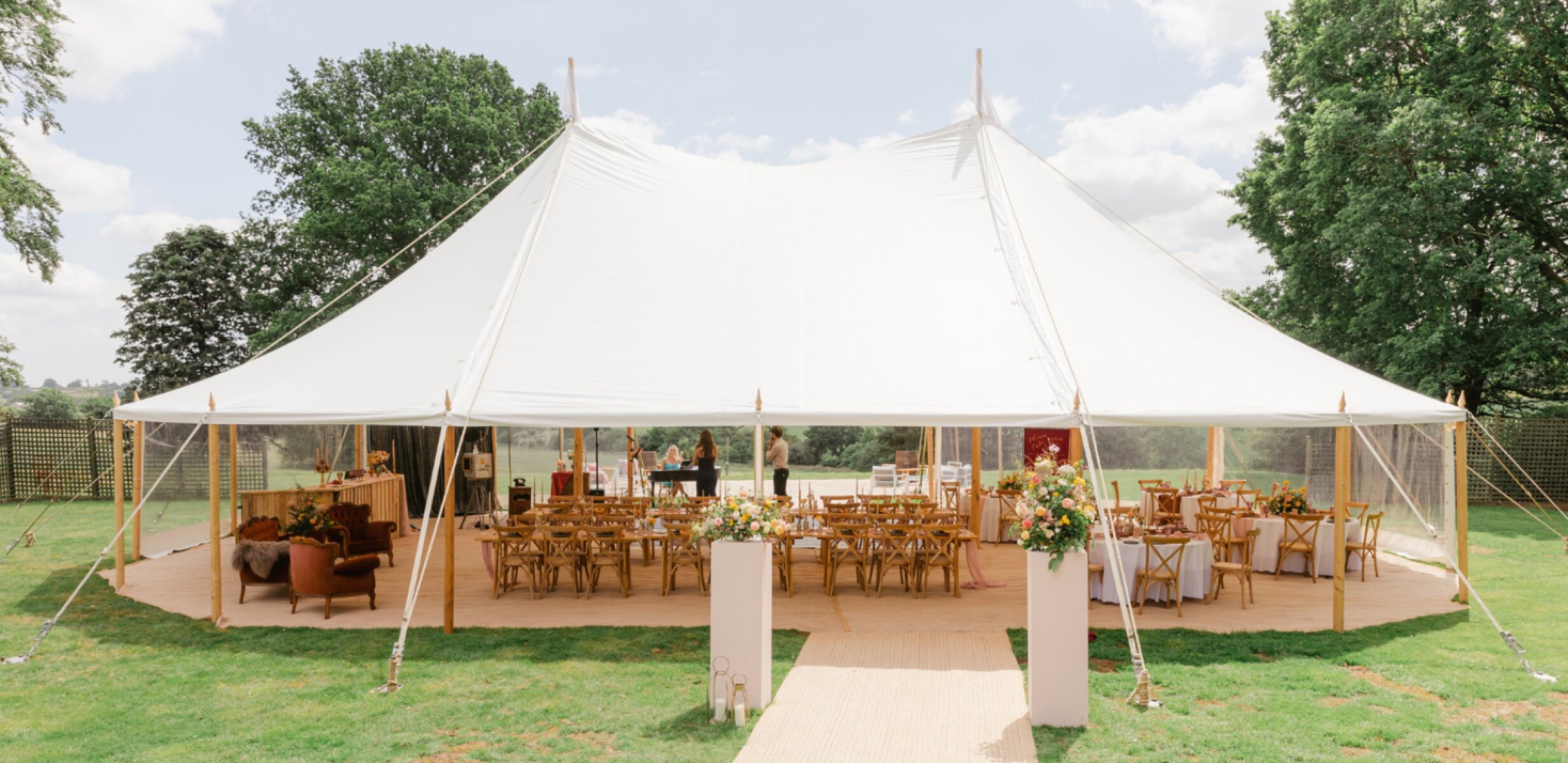 Elegant outdoor tent venue with wooden tables, surrounded by greenery, perfect for a stylish wedding celebration.