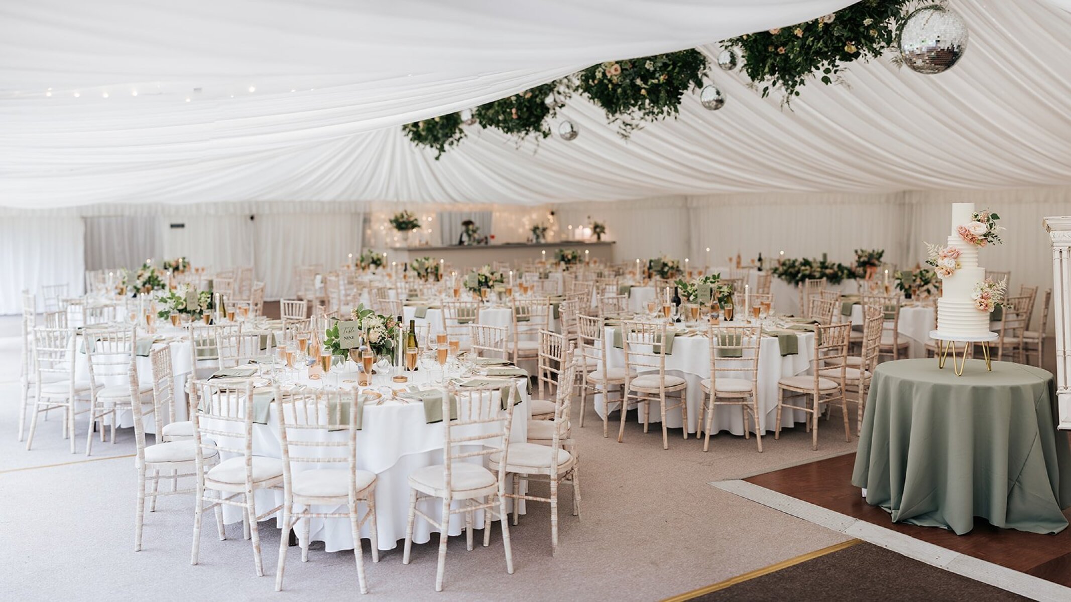 Elegant reception area featuring round tables adorned with floral centerpieces, surrounded by white drapery and a softly lit dance floor.