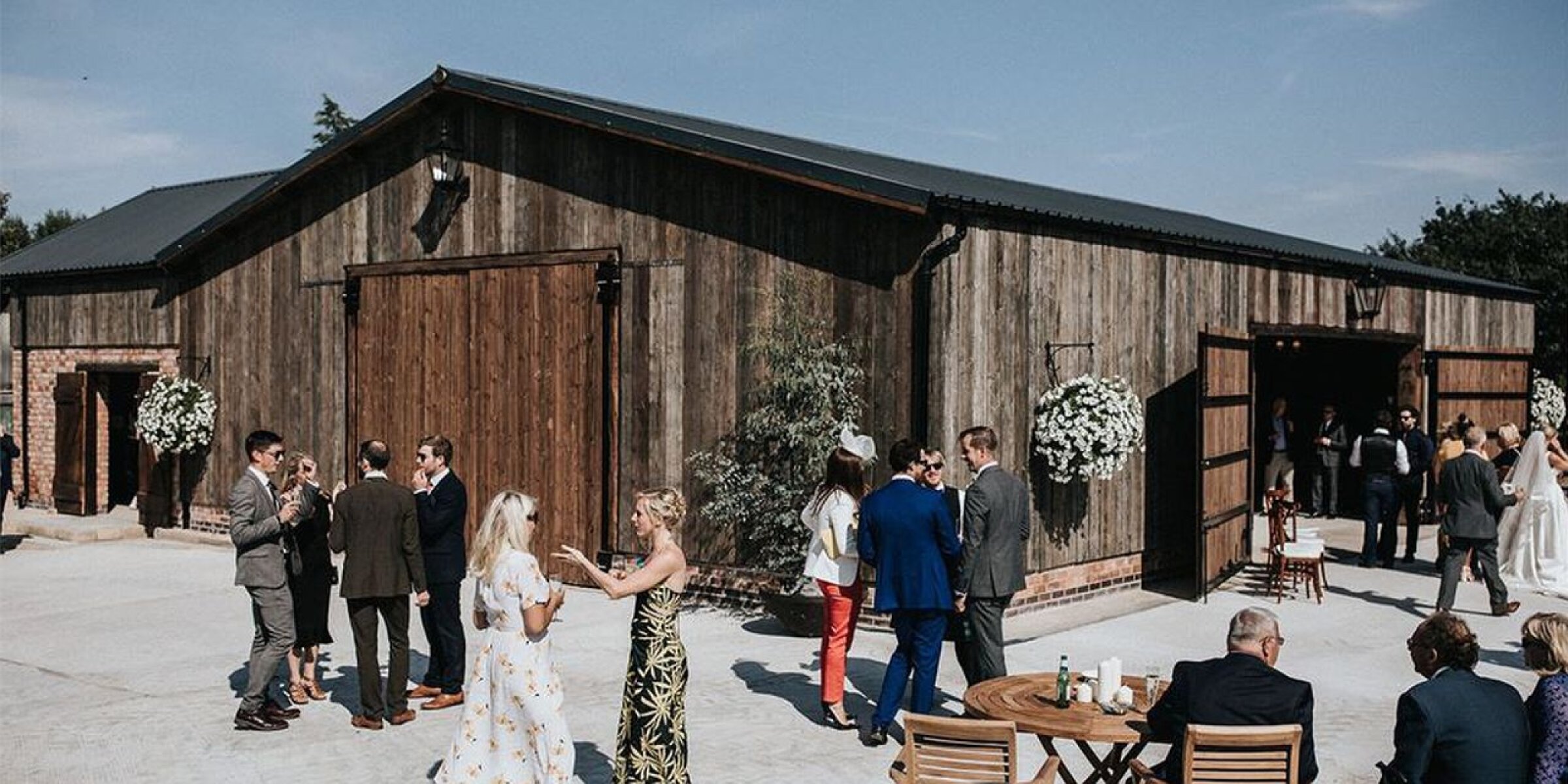 Rustic barn venue featuring a wooden exterior, guests mingling outdoors, and elegant floral arrangements adorning the entryway.