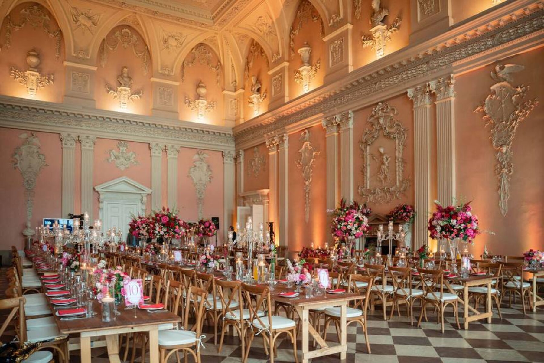 Grand ballroom featuring elegant pink walls, intricate moldings, and beautifully set tables adorned with floral centerpieces.