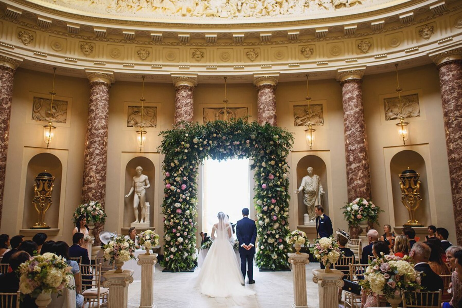 A stunning indoor ceremony space featuring marble columns, floral archway, and elegant seating, creating a romantic atmosphere for vows.