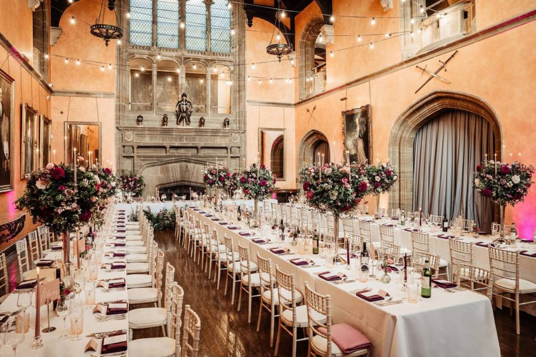 Elegant dining setup in a grand hall, featuring long tables adorned with floral centerpieces and soft hanging lights for a romantic ambiance.