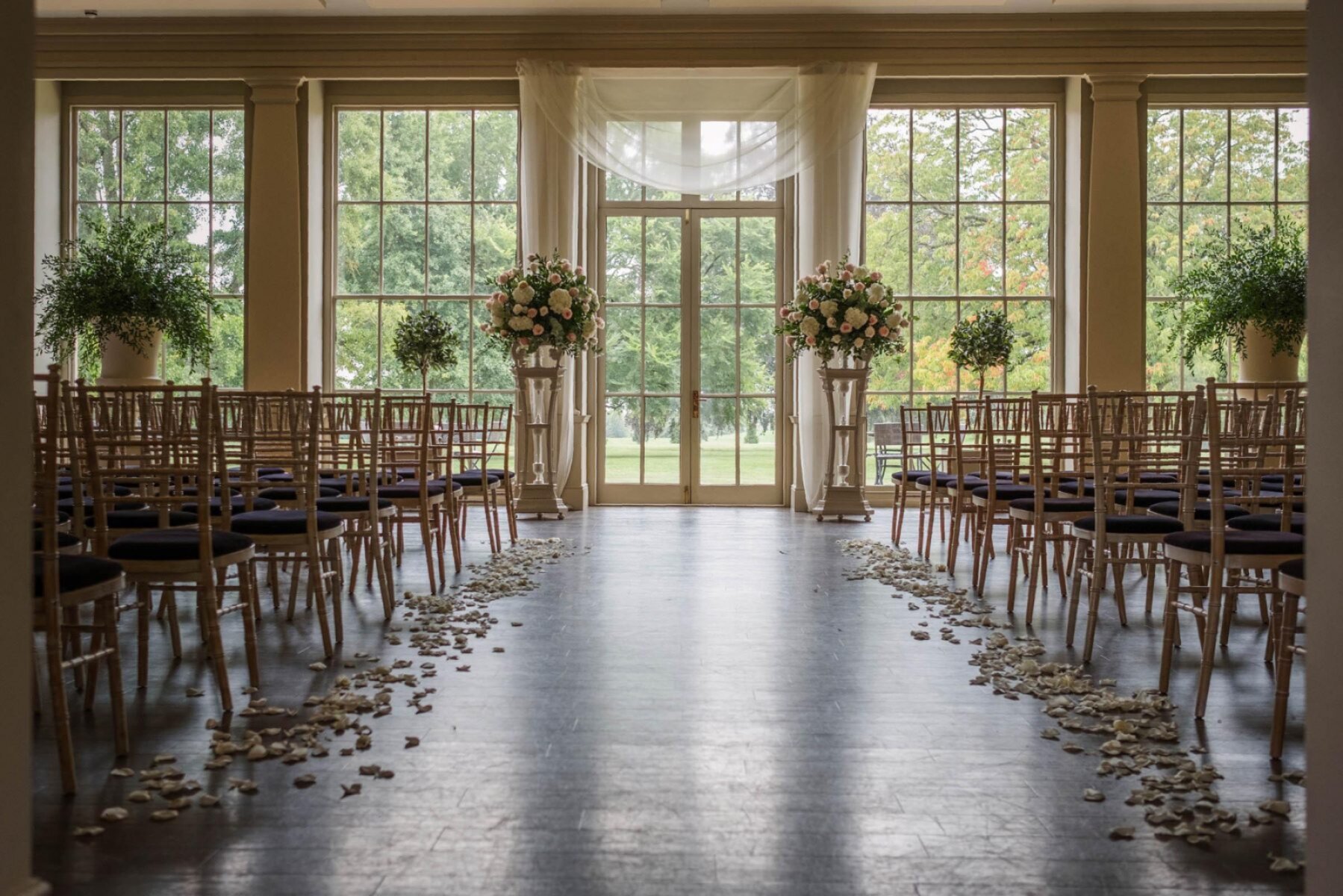 Elegant indoor ceremony space featuring rows of chairs, floral arrangements, and natural light streaming through large windows.