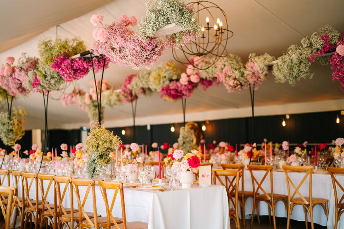 Elegant tented reception featuring long tables adorned with lush pink and white floral arrangements suspended overhead. Cozy, romantic atmosphere.