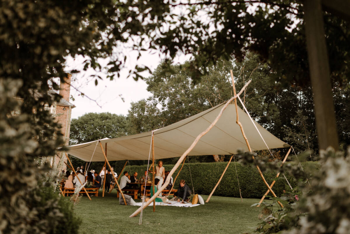 A spacious outdoor tent fills a lush green garden, set for a relaxed wedding celebration with guests enjoying the scenic surroundings.